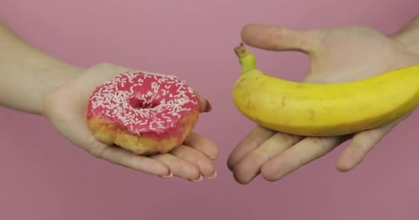 As mãos seguram donut e banana. Donut escolha contra banana. Alimentos saudáveis ou junk food — Vídeo de Stock