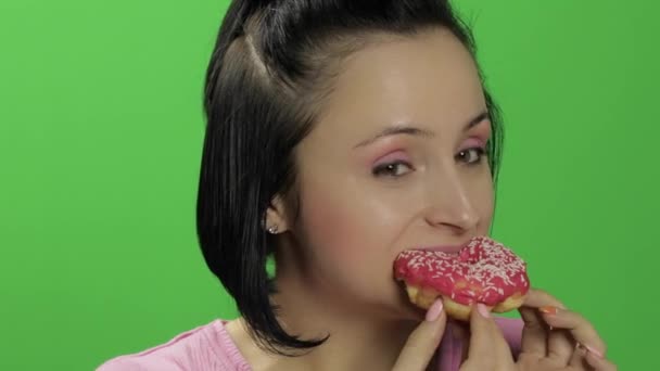 Όμορφη νεαρή γυναίκα με μεγάλη ευχαρίστηση τρώει ένα ντόνατ. Πλήκτρο αποχρώσεων — Αρχείο Βίντεο