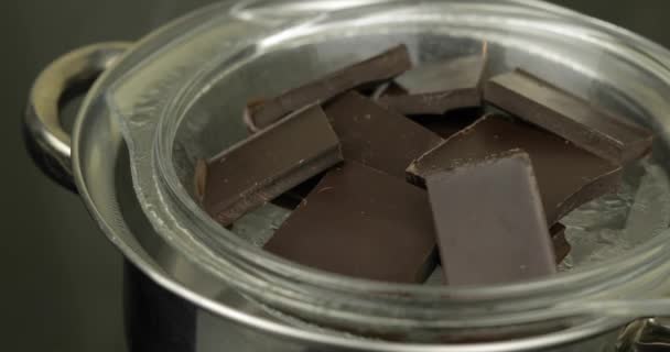 Таяние темного шоколада в миске положить в горячую кипяченую воду в кастрюлю на плите — стоковое видео