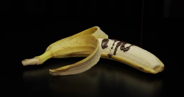 Pouring a banana with melted dark chocolate syrup. Black background — Stock Video