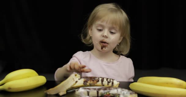 Çocuk muz yiyor, eritilmiş çikolata ve krem şanti ile çilek — Stok video
