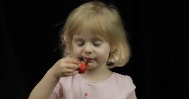 Kind met vuile gezicht van gesmolten chocolade en slagroom eet aardbei — Stockvideo