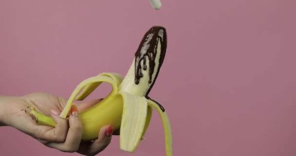 Verter un plátano con jarabe de chocolate negro derretido. Fondo rosa — Vídeos de Stock