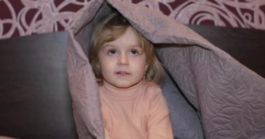 Küçük neşeli kız battaniye altında gizler ve Tv izlerken.