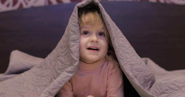 Weinig vrolijk meisje verbergt onder deken en tv kijken. concept van kinderen slapen — Stockvideo