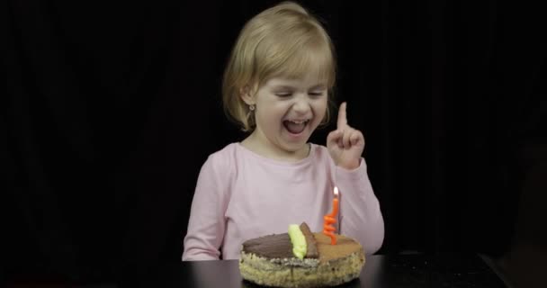 Pequena menina bonito sopra vela festiva no bolo de aniversário no fundo preto — Vídeo de Stock
