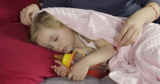 Genç anne uyurken küçük kızına göz kulak oluyor. Yataktaki kız — Stok video