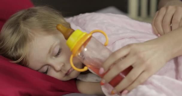 Niedliches Baby-Mädchen schläft auf gemütlichem Bett zu Hause und trinkt Saft aus der Flasche — Stockvideo