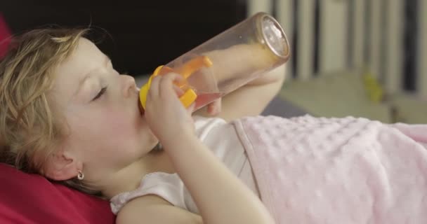 Menina bonito dormindo na cama aconchegante em casa e beber suco de garrafa — Vídeo de Stock