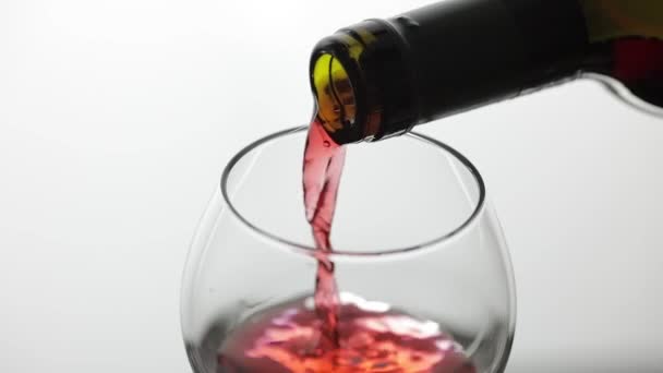 Ροζέ κρασί. Κόκκινο κρασί χύνουμε σε γυαλί κρασιού σε λευκό φόντο. Αργή κίνηση — Αρχείο Βίντεο