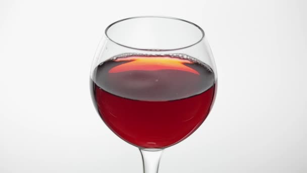 Gros plan d'une goutte tombant dans un verre avec du vin rouge. Vin rose sur fond blanc — Video