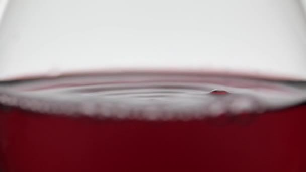 Gros plan d'une goutte tombant dans un verre avec du vin rouge. Vin rose sur fond blanc — Video