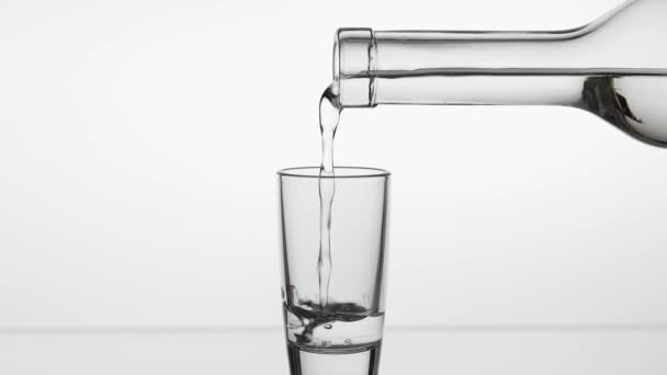 Een shot van wodka van een fles in glas gieten. Witte achtergrond — Stockvideo
