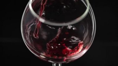Gül şarabı. Kırmızı şarap siyah arka plan üzerinde şarap cam dökün. Yavaş çekim