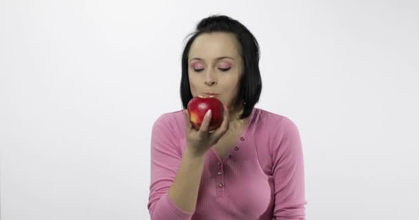 Young beautiful woman eating big, fresh and juicy red apple on white background — 비디오