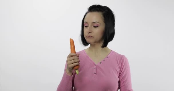 Jovem mulher bonita comendo cenoura grande no fundo branco e rir — Vídeo de Stock