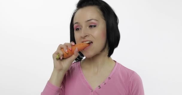 Молодая женщина ест морковку и говорит: "Ням". Девушка откусывает первый кусок и говорит: — стоковое видео