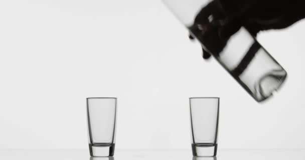 Derramar dois shots de vodka de uma garrafa em vidro. Fundo branco — Vídeo de Stock