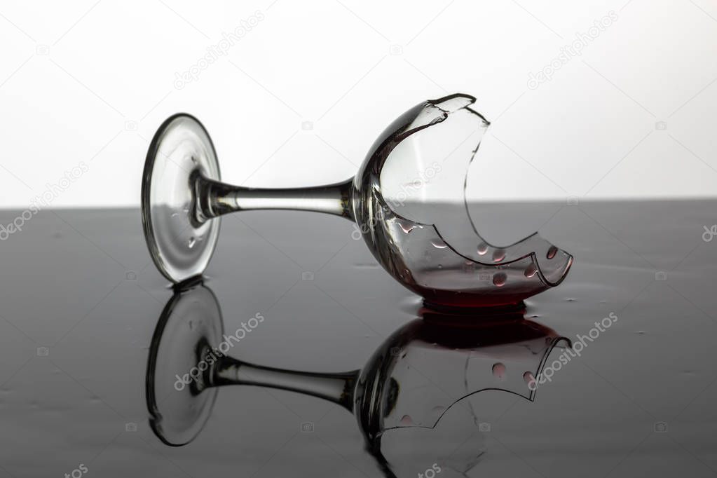 Broken wine glass with red wine which is laying on the wet surface