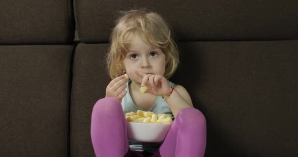 Meisje zittend op de Bank en het eten van maïs soezen. Kind glimlachend en proef puffcorns — Stockvideo