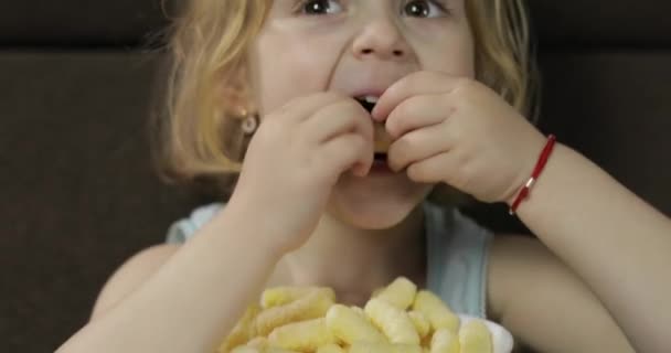 Kız kanepede oturuyor ve mısır lı puf yiyor. Çocuk gülümsüyor ve puf mısır tadı — Stok video