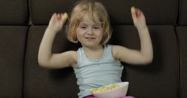 Chica sentada en el sofá y comiendo bocanadas de maíz. Niño viendo la televisión, degustar callos — Vídeos de Stock