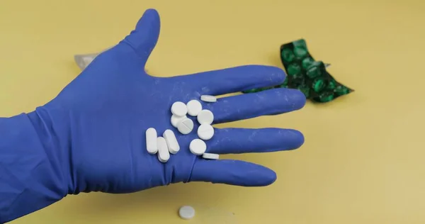 Большое количество белых таблеток в руке, одетых в резиновые стерильные медицинские перчатки — стоковое фото