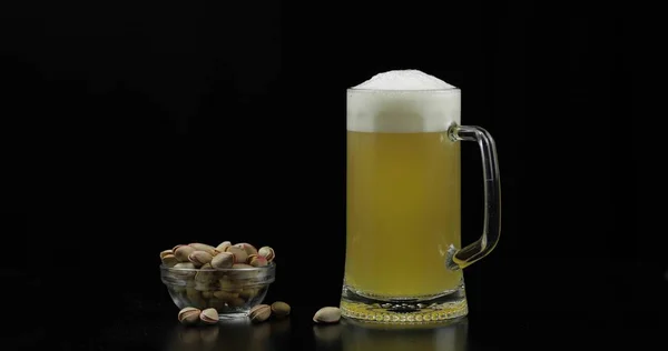 Cold Light Beer in a glass. Craft Beer close-up. Bowl of pistachios nuts.