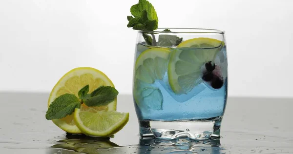 Glas med kall blå dryck med blad av mynta, lime, citron, svarta vinbär — Stockfoto