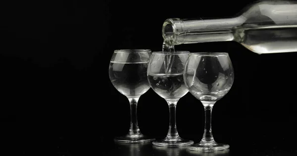 Выливание водки из бутылки в стакан на черном фоне — стоковое фото