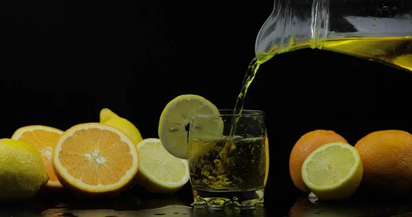 Vierta el jugo de la jarra en rodajas de vidrio, naranja y limón sobre el fondo —  Fotos de Stock