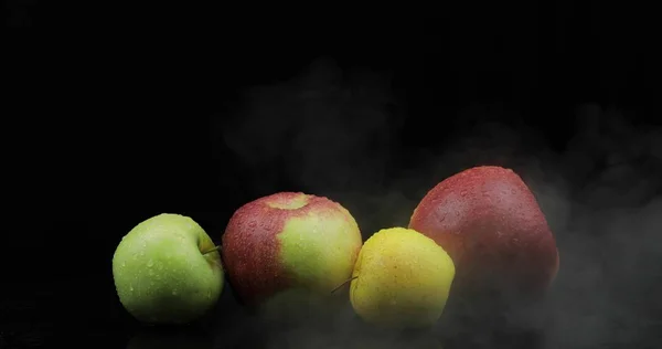 Manzana de frutas tropicales en hielo frío nubes de humo de niebla sobre fondo negro — Foto de Stock