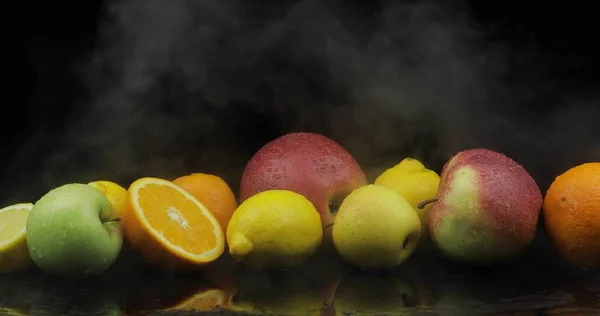 Limón tropical, naranja, manzana en hielo frío nubes de humo de niebla sobre fondo oscuro — Foto de Stock