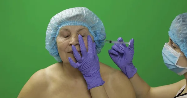 Mujer anciana con sombrero protector. Médico haciendo inyecciones faciales para el paciente — Foto de Stock
