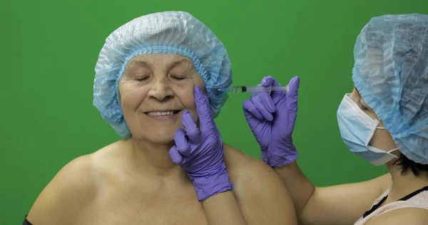 Mujer anciana con sombrero protector. Médico haciendo inyecciones faciales para el paciente — Foto de Stock