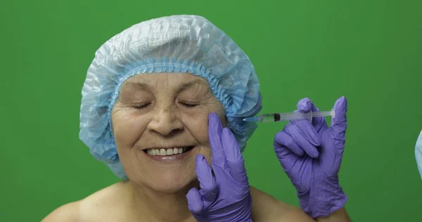 Mujer anciana con sombrero protector. Médico haciendo inyecciones faciales para el paciente — Foto de Stock