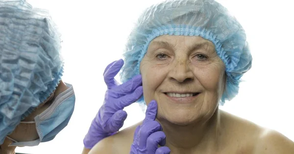 Mujer anciana sonriente con sombrero protector. Cirujano plástico mirando cara mujer — Foto de Stock