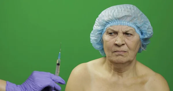 Mujer anciana sonriente con sombrero protector asustada de la jeringa con medicamentos — Foto de Stock