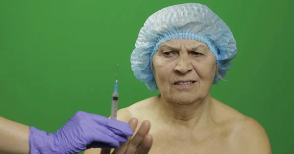 Mujer anciana sonriente con sombrero protector asustada de la jeringa con medicamentos — Foto de Stock