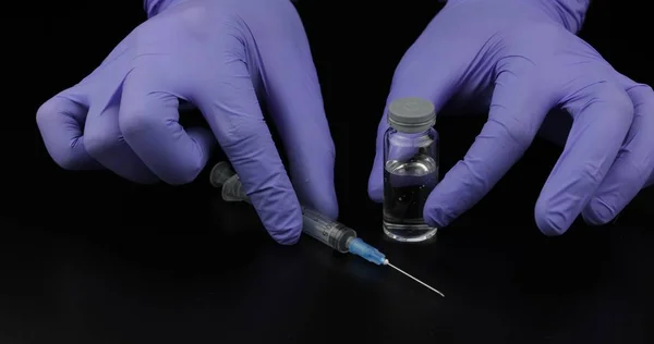 Doktoři si rukou stříkačku, ampuli s očkováním na černém pozadí — Stock fotografie