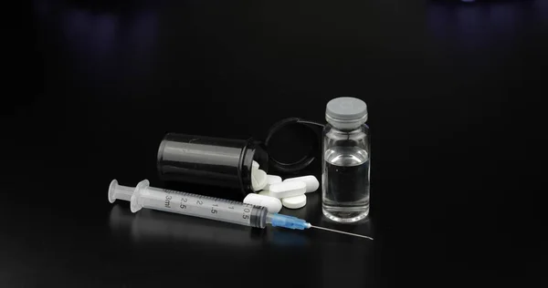 Pastillas, jeringa y ampolla con vacunación sobre fondo negro — Foto de Stock