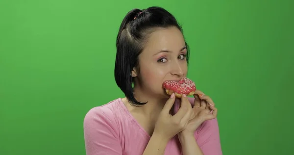 Красивая молодая женщина с большим удовольствием ест пончик. Ключ хрома — стоковое фото