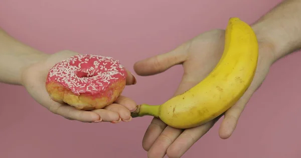 Las manos sostienen la dona y el plátano. Elección de la dona contra el plátano. Comida sana o chatarra — Foto de Stock