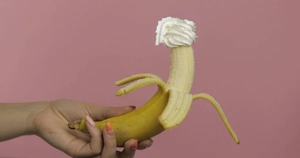 Donna mano tiene banana con panna montata sulla parte superiore del frutto — Foto Stock