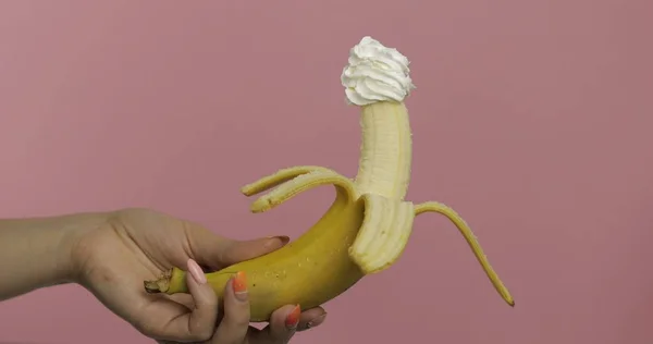 Mulher mão segura banana com chantilly em cima da fruta — Fotografia de Stock