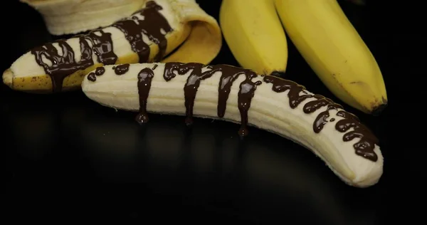 Banana com xarope de chocolate escuro derretido. Fundo preto — Fotografia de Stock