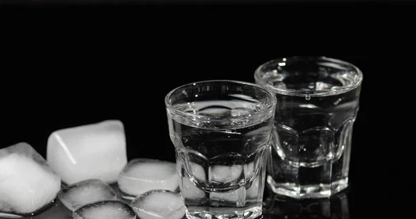 Vodka en vasos de chupito con cubitos de hielo colocados sobre fondo negro — Foto de Stock