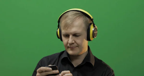 Guy listens to music in wireless yellow headphones. Green screen