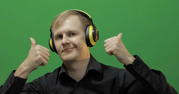 Guy listens to music in wireless yellow headphones and dances. Green screen
