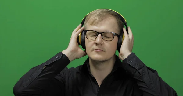 Ο τύπος ακούει μουσική με ασύρματα κίτρινα ακουστικά και χορούς. Πράσινη οθόνη — Φωτογραφία Αρχείου